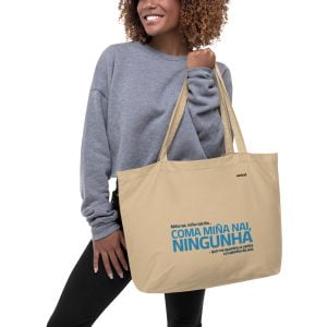 Una mujer sonriente llevando una bolsa de tela grande de color beige con texto impreso.